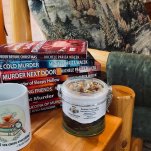 Charlie's Concoctions Lemon Lavender tea tin and "A cup of tea cures everything" mug beside a stack of Charlie Kingsley Mystery books by Michele Pariza Wacek on a rustic wooden chair