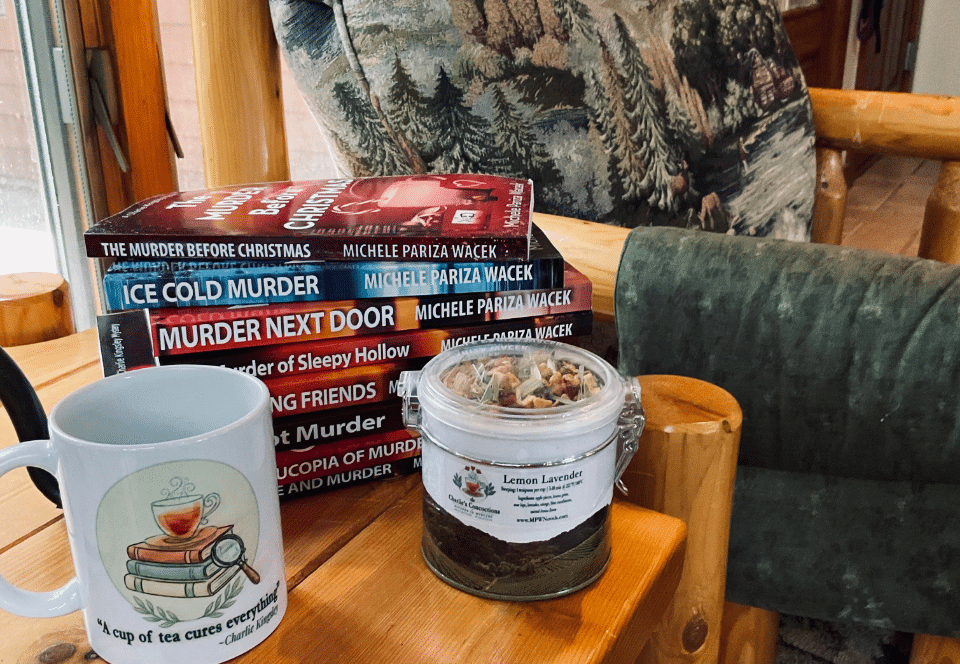 Charlie's Concoctions Lemon Lavender tea tin and "A cup of tea cures everything" mug beside a stack of Charlie Kingsley Mystery books by Michele Pariza Wacek on a rustic wooden chair