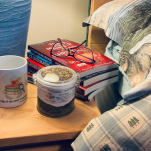 Charlie's Concoctions Deep Sleep tea tin and "A cup of tea cures everything" mug on a bedside table, with a stack of Charlie Kingsley Mystery books by Michele Pariza Wacek and reading glasses nearby