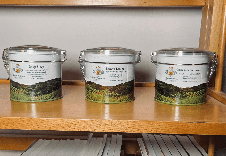 Three Charlie's Concoctions tea tins on a wooden shelf: Deep Sleep, Lemon Lavender, and Candy Cane Concoction